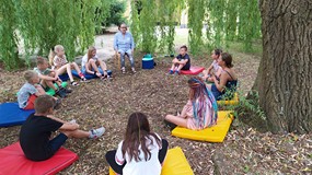Pogadanka o przyrodzie. Dzieci i prowadząca zajecia siedzą w ogrodzie