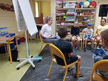 Dzieci podczas zajęć słuchają wskazówek prowadzącej dotyczących kompozycji, kształtów oraz kolorów