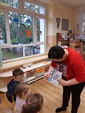 Bibliotekarka pokazuje dzieciom kartę czytelnika i pakiet startowy dla przedszkolaków