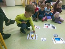 Chłopiec dopasowuje obrazek do odpowiedniego bohatera bajki; w tle grupa dzieci