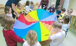 Dzieci stoją w kole. Każde z nich trzyma kolorową chustę Klanzy