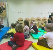 Dzieci podczas zajęć bibliotecznych słuchają opowiadania czytanego przez bibliotekarkę