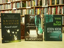 na tle regałów bibliotecznych stoją trzy książki: 