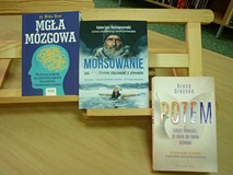 na tle regałów leżą książki: 