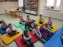 Dzieci siedzą na kolorowych materacach i słuchają opowiadań