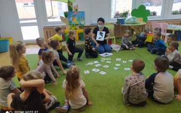 Bibliotekarka pokazuje dzieciom obrazek z cieniem postaci bajkowej.