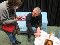 Przemysław Piotrowski składa autograf na książce.