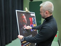 Przemysław Piotrowski podpisuje plakat.