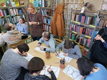 Uczestnicy siedzą przy stolikach podczas tworzenia pracy plastycznej