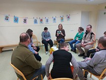 Uczestnicy siedzą na krzesłach, słuchając ksiazki