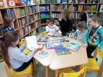 Dzieci siedzą przy stole i oglądają książeczki oraz układają puzzle