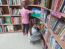 Dwie dziewczynki stoją przy regale z książkami i szukają ulubionej bajki