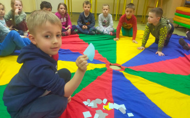 Chłopiec pokazuje symbol wielkanocny. Dzieci siedzą na kolorowej chuście