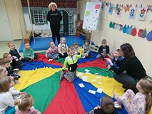 Dzieci podczas zajęć siedzą w kole na kolorowej chuście i wspólnie rozmawiają