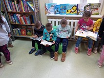 Dzieci siedzą na materacykach i oglądają książeczki