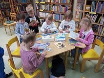 Dzieci siedzą przy stole i oglądają książeczki oraz układają puzzle