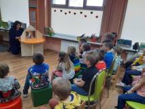 Dzieci słuchają i oglądają papierowy teatrzyk Kamishibai.