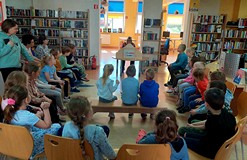 Na zdjęciu przedszkolaki siedzą na krzesełkach i słuchają 