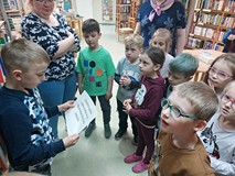 Chłopiec stoi i czyta wskazówkę, a pozostałe dzieci słuchają