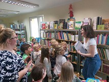 Dzieci stoją i patrzą na zagadki prezentowane przez bibliotekarkę