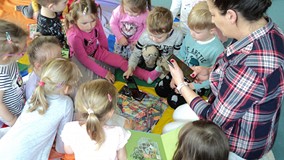 dzieci wraz z bibliotekarką oglądają książkę o dinozaurach