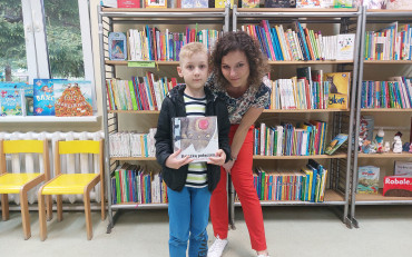 Chłopiec pozuje z książeczką i bibliotekarką