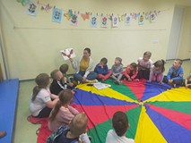 Dzieci siedzą na kolorowej chuście animacyjnej i słuchają opowiadania