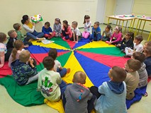 Dzieci siedzą na kolorowej chuście animacyjnej i słuchają opowiadania