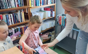 Dziecko, z pomocą bibliotekarki, skanuje kod kreskowy z książki