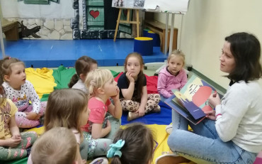 Dzieci podczas zajęć  na kolorowej chuście i słuchają opowiadania, czytanego przez...