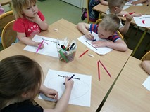 Dzeici siedzą przy stolikach i kolorują laurki