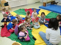 Dzieci siedzą na kolorowej chuście animacyjnej i słuchają opowiadania