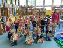 dzieci wraz z bibliotekarką pozują do zdjęcia z książkami od Miejskiej Energetyki Cieplnej