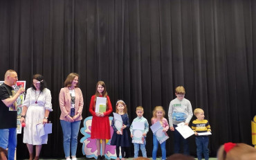 Dzieci wraz z bibliotekarką stoją na scenie i prezentują nagrody