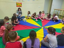 Dzieci siedzą na kolorowej chuście animacyjnej i słuchają opowiadania