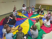 Dzieci siedzą na kolorowej chuście animacyjnej i rozmawiają