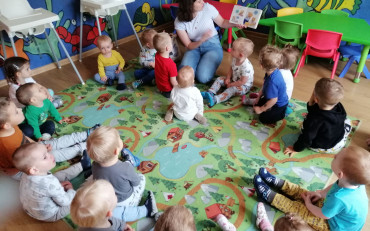 Bibliotekarka czyta dzieciom książkę, dzieci siedzą na kolorowym dywanie