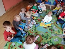 Dzieci siedzą na kolorowym dywanie i oglądają książeczki