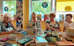 Panie siedzą przy stole i wybierają najciekawsze pozycje z nowości wydawniczych