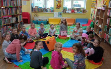 Dzieci siedzą w okręgu na chuście animacyjnej podczas zabawy.