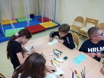 Dzeici siedzą przy stolikach i wykonują pracę plastyczną