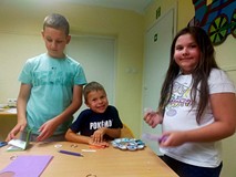 Dzeici siedzą przy stolikach i wykonują pracę plastyczną