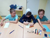 Dzeici siedzą przy stolikach i wykonują pracę plastyczną