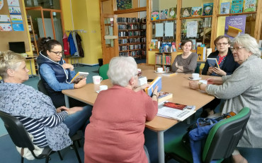 uczestniczki dkk wraz z bibliotekarką siedzą przy stole i dyskutują o książce