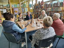 uczestniczki dkk wraz z bibliotekarką siedzą przy stole i dyskutują o książce