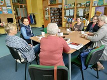 uczestniczki dkk wraz z bibliotekarką siedzą przy stole i dyskutują o książce