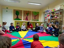 Dzieci siedzą na kolorowej chuście animacyjnej i rozmawiają o skarbach jesieni