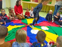 Dzieci siedzą w kole na kolorowej chuście i przyporządkowują obrazki