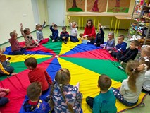 Dzieci siedzą na kolorowej chuście animacyjnej i rozmawiają o skarbach jesieni