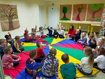 Dzieci siedzą na kolorowej chuście animacyjnej i rozmawiają o skarbach jesieni